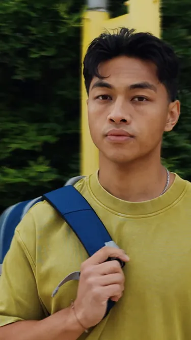 Mann im gelben T-Shirt mit blauem Rucksack über der Schulter.